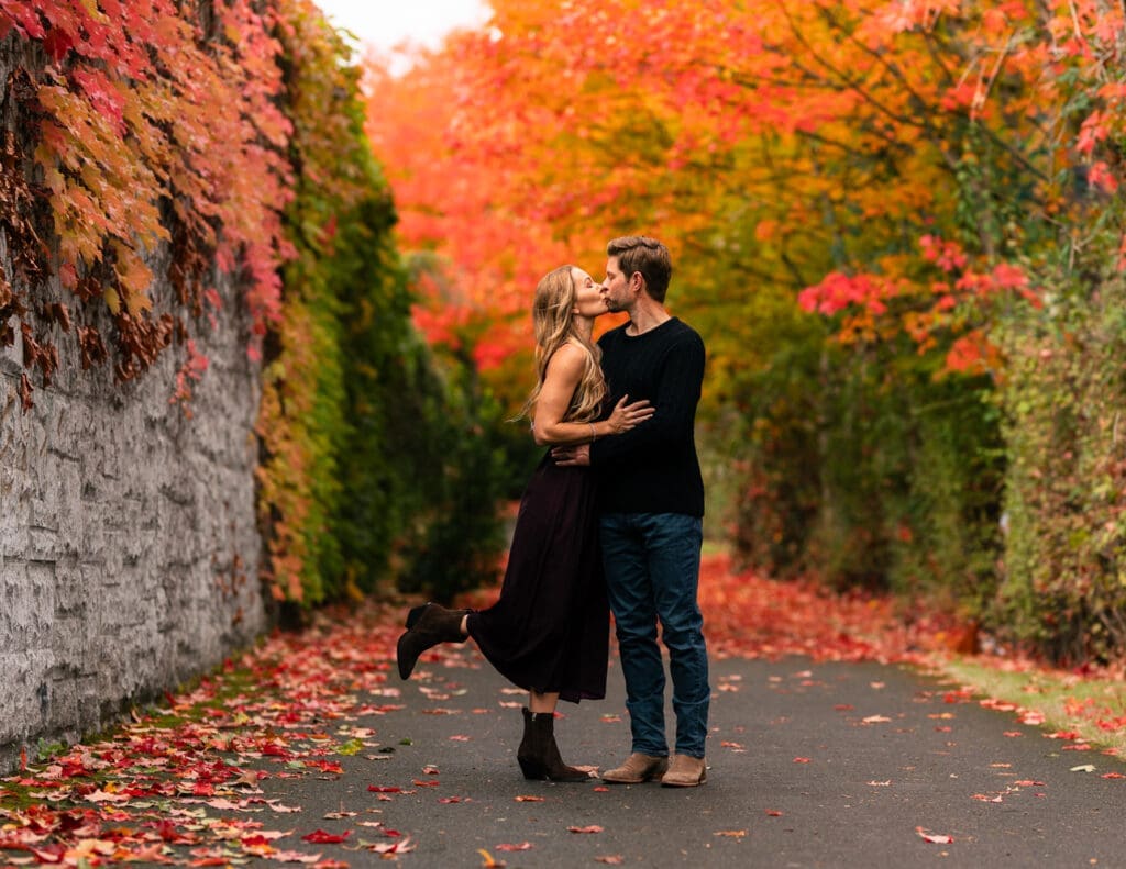 Parents shown kissing during a fall family photoshoot on Seattle's Eastside in peak autumn season. Fall foliage behind them is stunning and vibrant. Taken by Maë Lans Photography.
