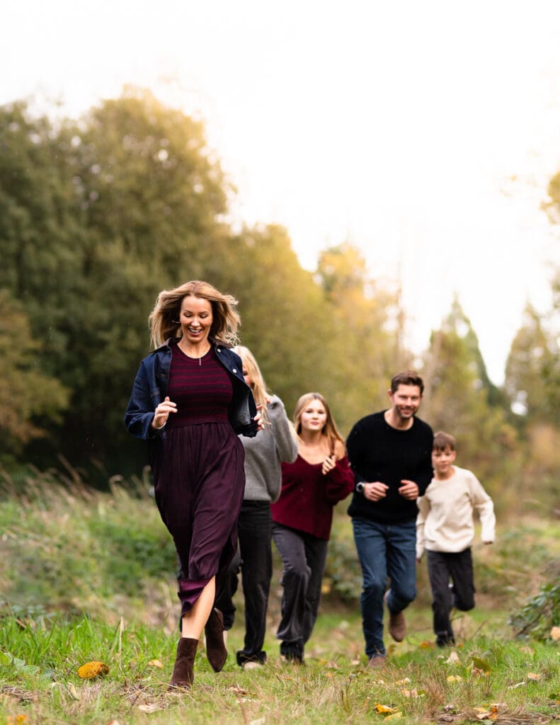 Fall family photoshoot on Seattle's Eastside along West Lake Sammamish. Shown here is a family running through a grassy field as they are portrayed with Maë Lans Photography's classic golden hues and timeless imagery.