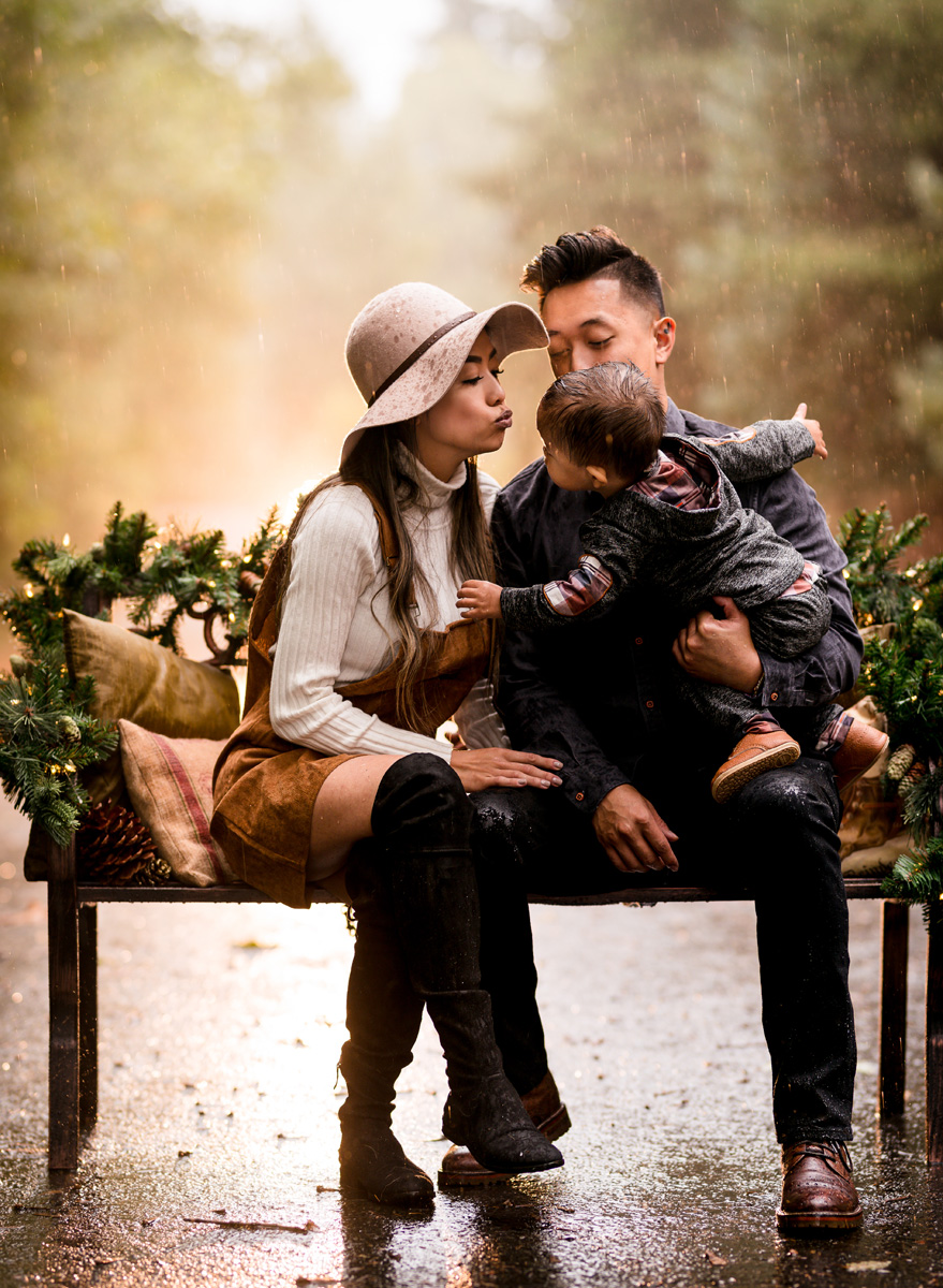 A family shown seated on a holiday bench during their family photoshoot. Image shows rich colors and golden glows characteristic of Maë Lans Photography's photography style.