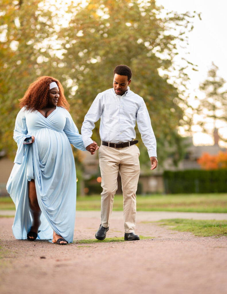 Father-to-be holding his wife's hand in a beautiful Redmond, Washington park. She is close to 9 months pregnant and wearing a gorgeous, blue maternity dress.