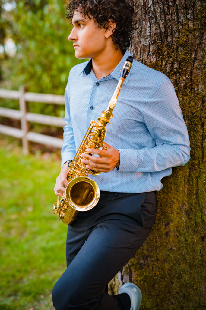 Photograph of a senior in high school and his saxophone leaning against a tree at a park in Redmond, WA during his senior photoshoot.