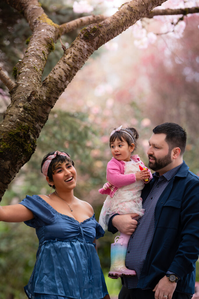 Family of three during their cherry blossom photo session against a gorgeous bokeh of cherry blossom branches.
