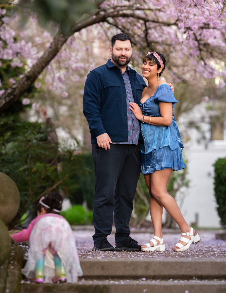 Parents are shown together enjoying  watching their daughter climb up stairs, under cherry blossom arches in Bellevue, Washington.