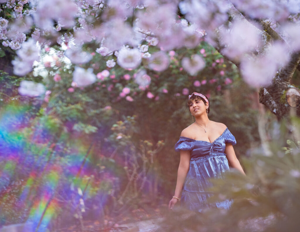 Mom pictured in a dreamy like setting under a cherry blossom bokeh and artistic rainbow effect shown in this portrait photograph taken in Bellevue, WA.