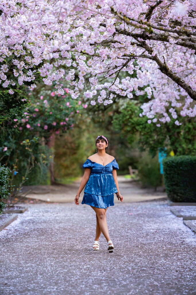 Mom walking down a path lined with cherry blossom trees and Bellevue Downtown Park, during her portrait photoshoot session.